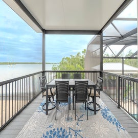 Your covered terrace offers perfect outdoor dining with stunning water views beyond the lush greenery.