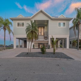 Modern beachside home featuring elevated design with palm trees and tropical landscaping in a serene coastal setting.