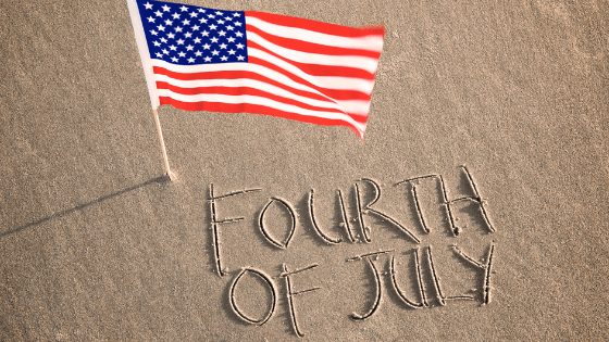 Fourth of July written in sand with flag